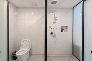 Une salle de bain moderne équipée de toilettes, d’une douche et d’une petite étagère où sont rangés les articles de toilette.