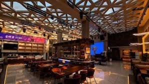 Ein modernes Restaurant mit einem geometrischen Deckenbau, mehreren Sitzbereichen und einer Bar.
