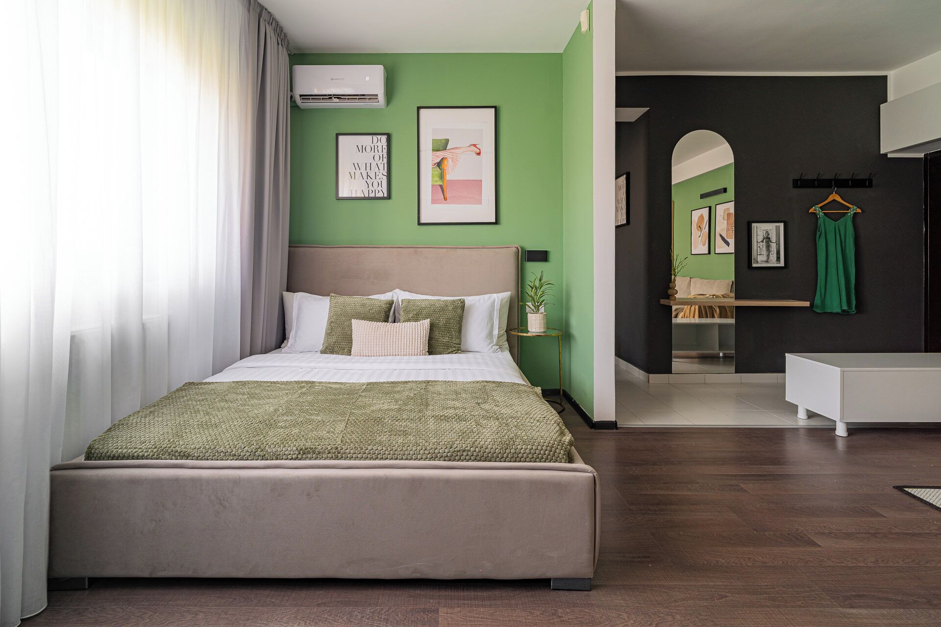 A modern bedroom with a large bed, green walls, and a view into another room.
