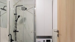 A compact bathroom with a glass-enclosed shower, a sink, a toilet, and a built-in washing machine. - Cismigiu Park Studio - Fresh & Serene Flat with Light-Filled Interiors (Bucharest)