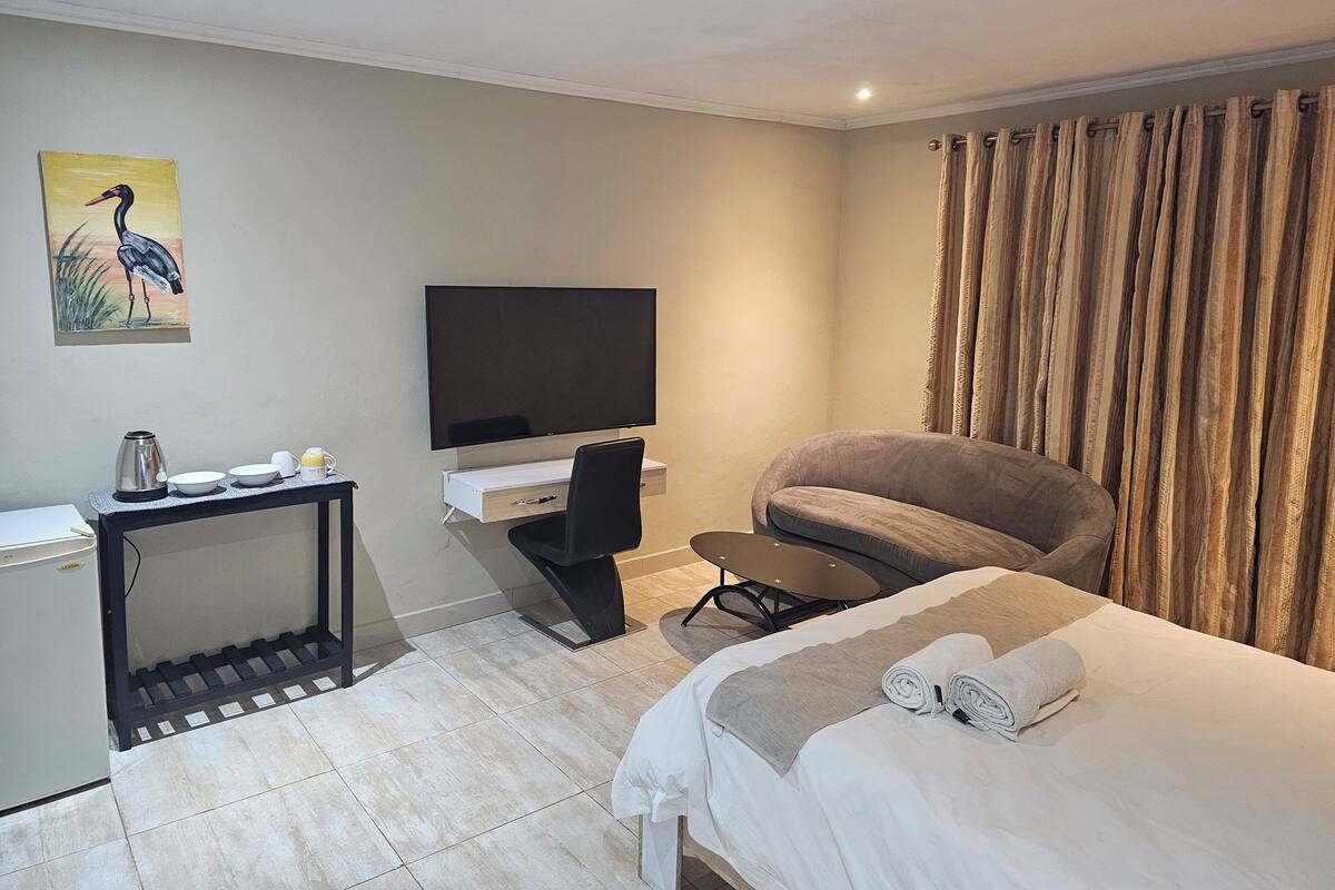 Una habitación de hotel con una cama, un escritorio con televisión, una silla y una cortina.