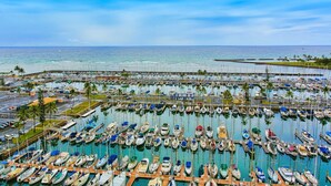 Un puerto deportivo con numerosas embarcaciones amarradas en aguas tranquilas, rodeado de un cielo despejado y palmeras.
