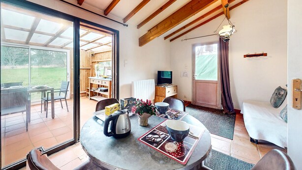 Una habitación acogedora con una mesa de comedor, sillas, un televisor y un ventanal corredero que da a un espacio exterior.