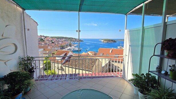 Un balcone con vista su una cittadina costiera, una piscina e piante in vaso.