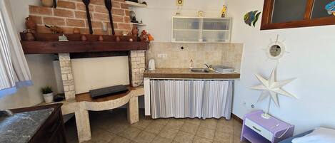 Una cocina con pared de ladrillo, estantes de madera, estufa y ventana con cortinas.