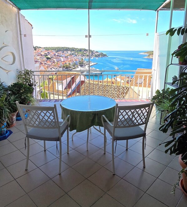 A balcony with a table and chairs, overlooking a coastal town and the sea. - Bocin Rosso Apartments II (Hvar)