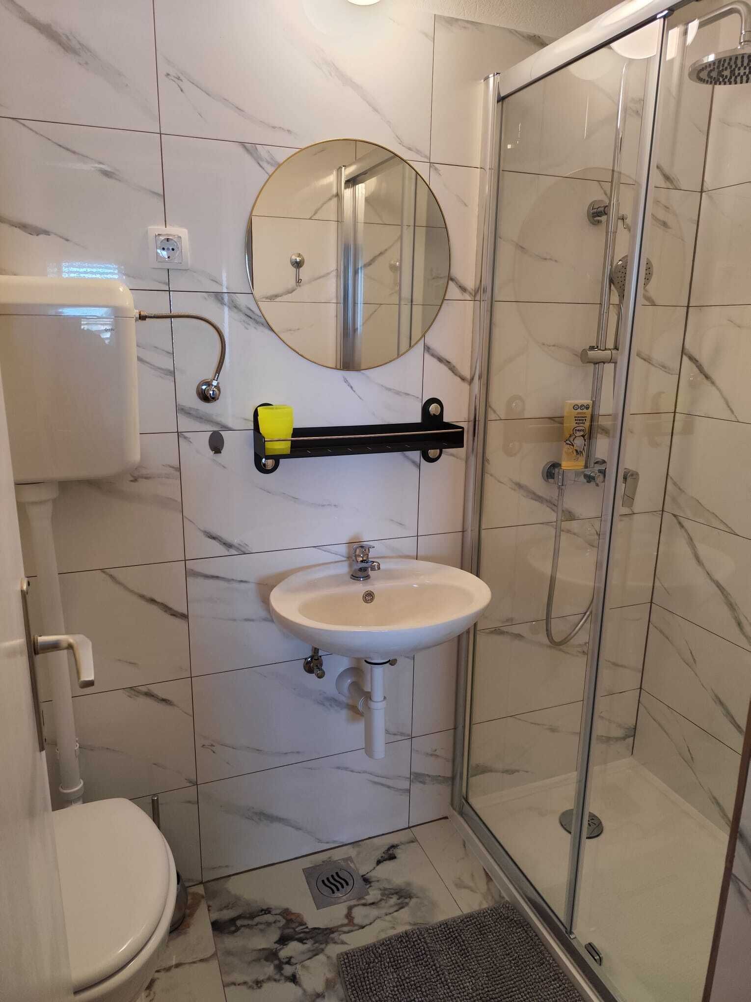 Uma casa de banho com sanita, lavatório, espelho e chuveiro.