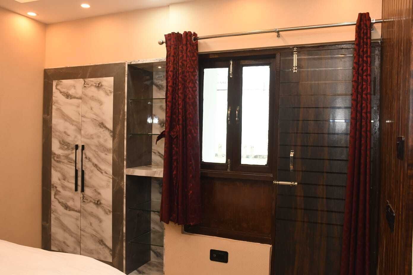 A bedroom with a marble wardrobe, a dark wooden door, and a window with curtains.