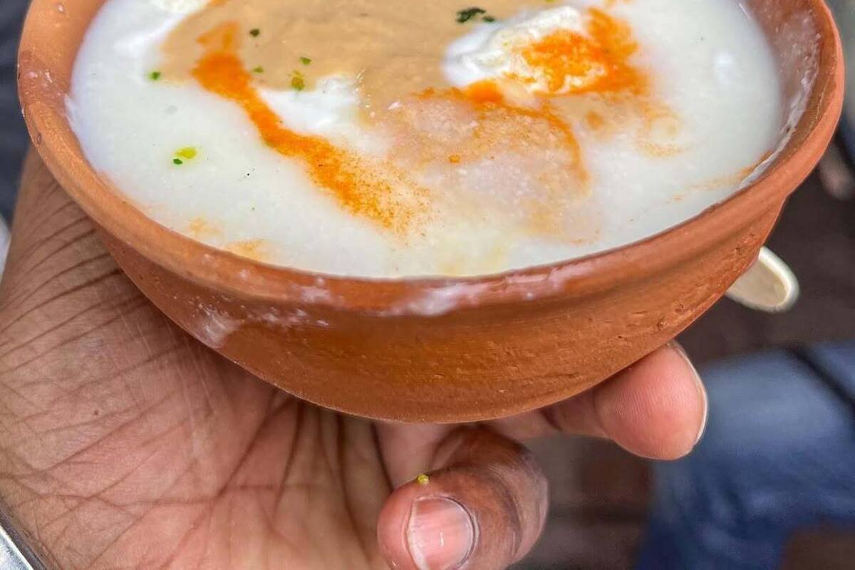Una mano sosteniendo un plato de comida con una base cremosa blanca y un topping marrón, adornado con hierbas verdes.