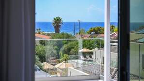 Un balcon avec vue sur l’océan, des palmiers et un espace piscine équipé de chaises longues et de parasols.