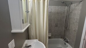 Un baño con ducha, lavamanos y espejo.
