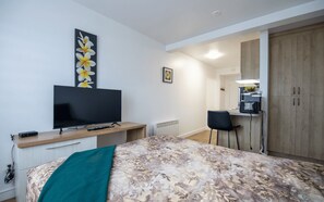 A modern hotel room with a large bed, a flat-screen TV, a desk with a chair, and a wardrobe. - Appartements-Hôtel les Mouettes (Sept-Îles)