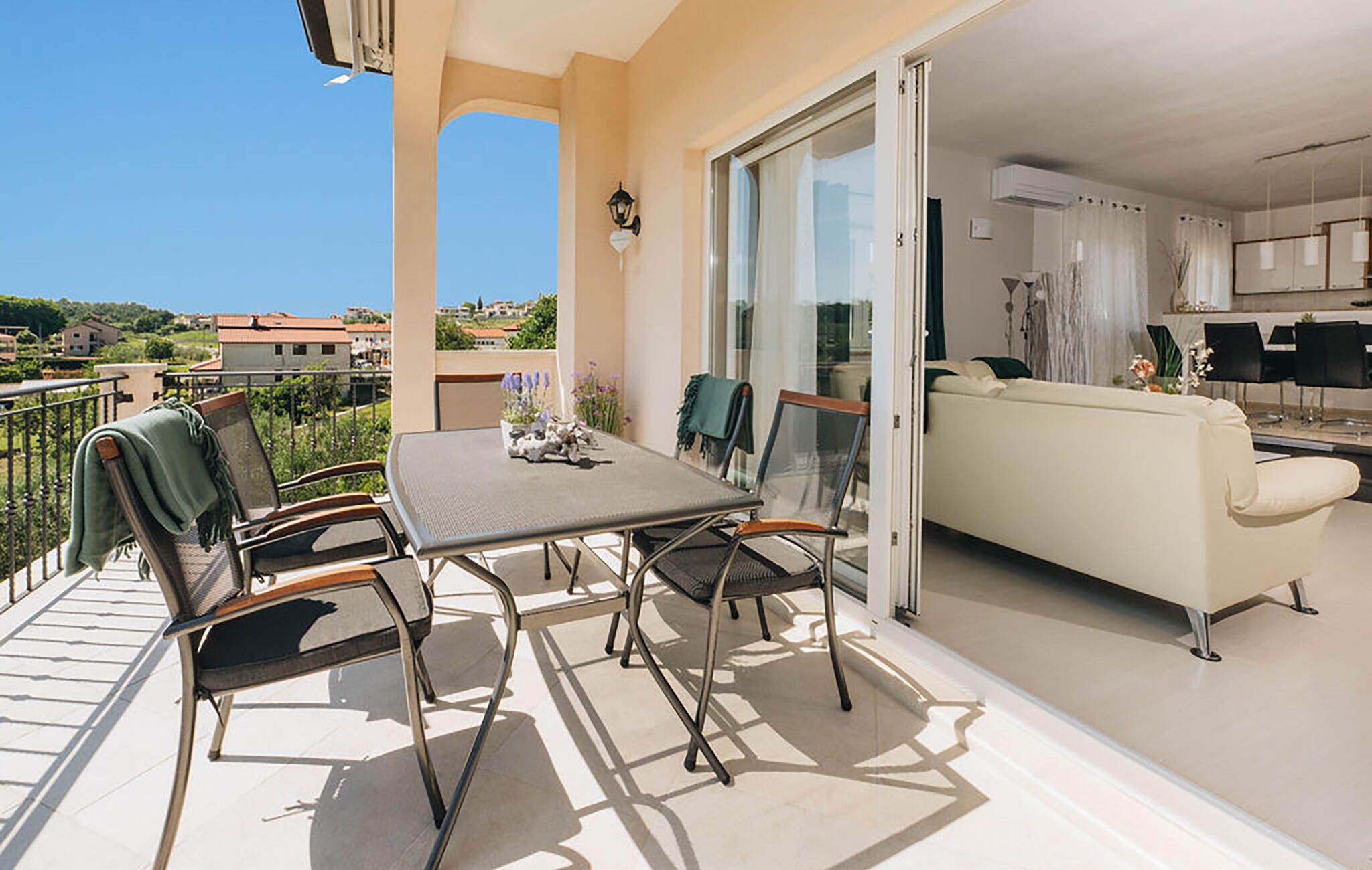 A balcony with a table and chairs, a sofa, and a sliding glass door leading to a kitchen.