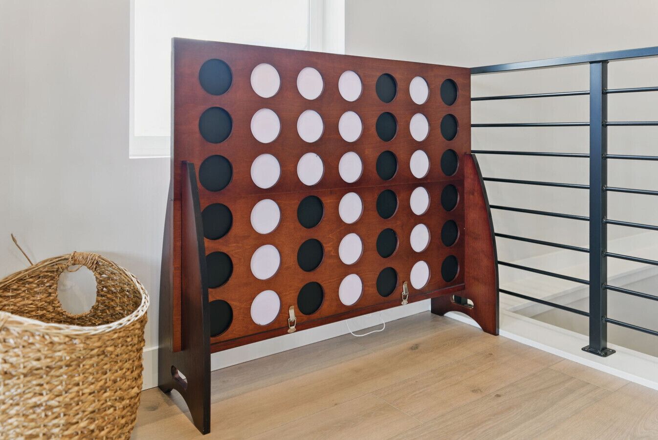 A wooden pegboard with circular holes, a metal railing, and a wicker basket on a wooden floor.