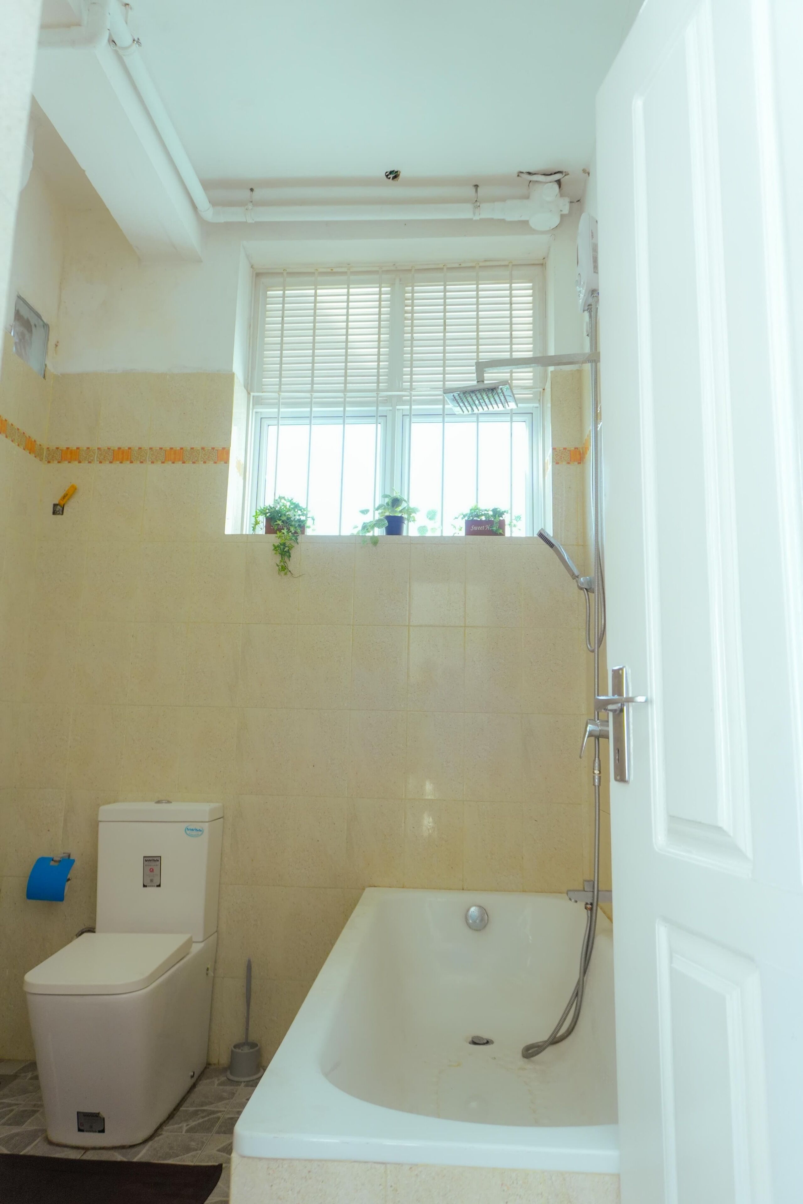 A bathroom with a bathtub, toilet, and window with plants.