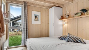 Un dormitorio con cama, armario, ventana con cortinas, lámpara de noche y vistas al exterior.