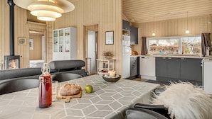 Un acogedor interior de cabaña con comedor, cocina y una estufa de leña a la vista.