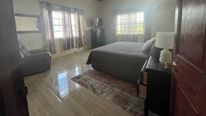 Una camera da letto con un letto, una cassettiera, una sedia, una TV e una finestra con tende.