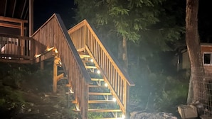 A wooden staircase leading to a deck with railings, surrounded by trees and rocks. - Riviera - A gathering spot (Lansdowne)