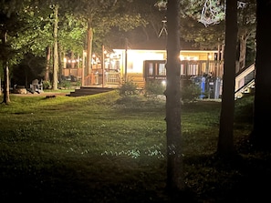 Un espacio exterior bien iluminado con terraza de madera, escalones que conducen a un edificio y un césped.
