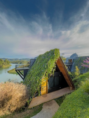 A modern house with a sloped roof covered in greenery, a wooden deck, and a view of a lake and mountains. - GRETEL CHALETS SUIZO (Guatapé)