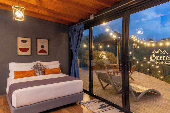 A bedroom with a bed, a window, and a view of an outdoor deck. - GRETEL CHALETS SUIZO (Guatapé)