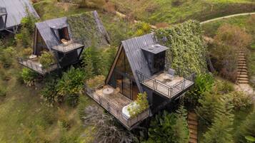 Tres cabañas estilo casa del árbol con asientos exteriores y un cerramiento de cristal, rodeadas de abundante vegetación.