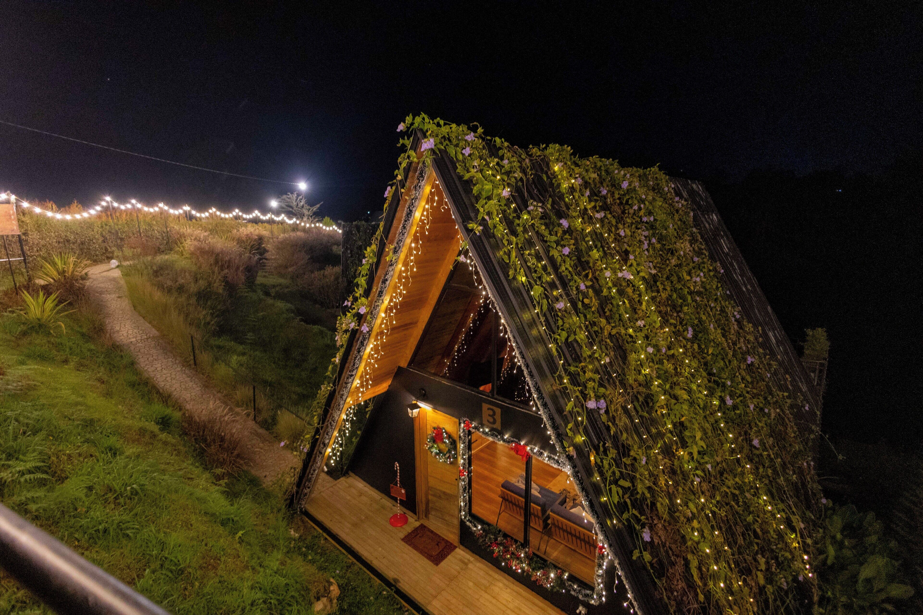 A small, A-frame structure with a wooden deck and a single room with a bed and a nightstand.