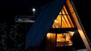 Una cabaña de madera triangular con un ventanal grande y un balcón.