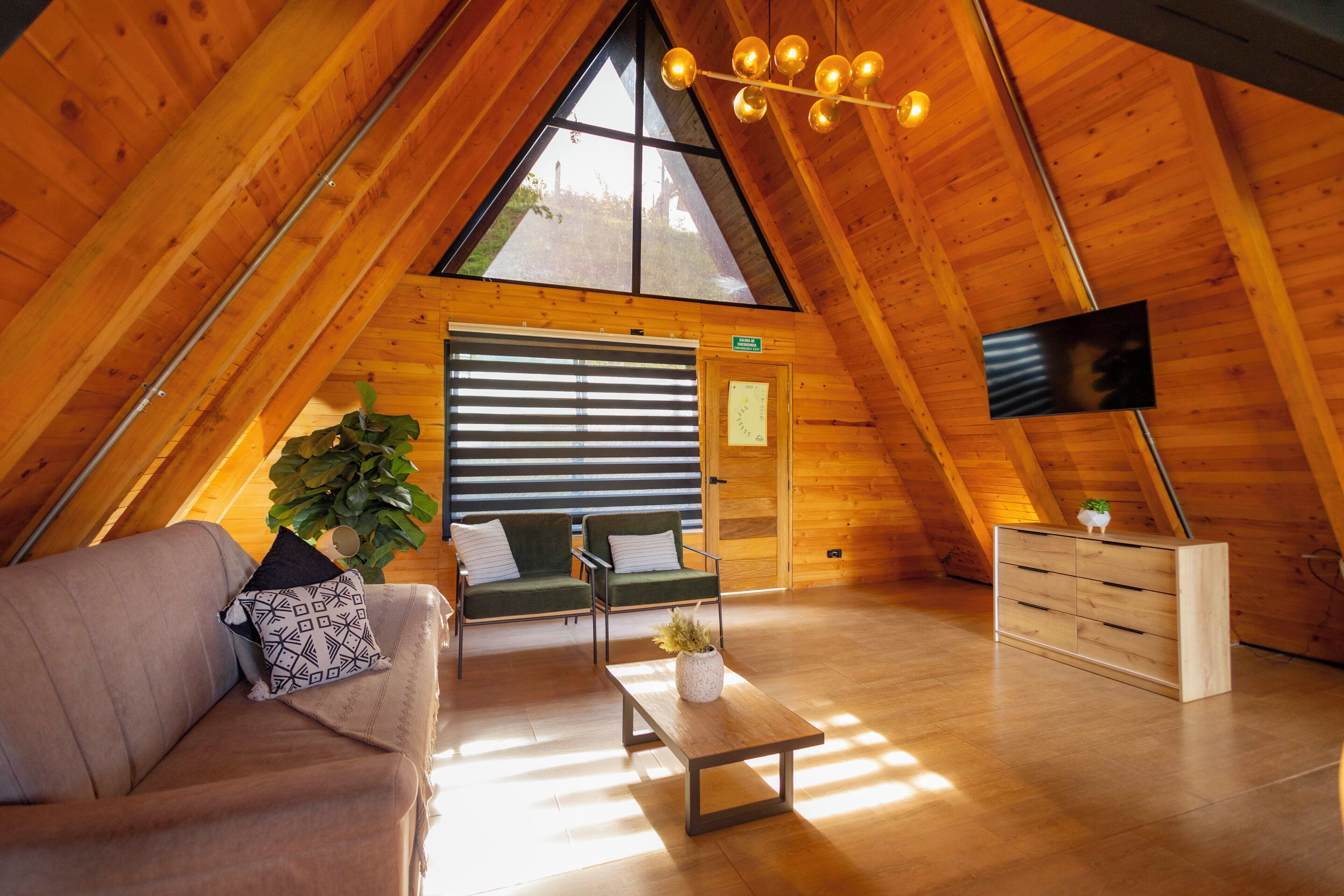 Ein gemütlicher, holzgetäfelter Innenraum mit schrägem Dach, einer Couch, einem Couchtisch und einem an der Wand befestigten Fernseher.