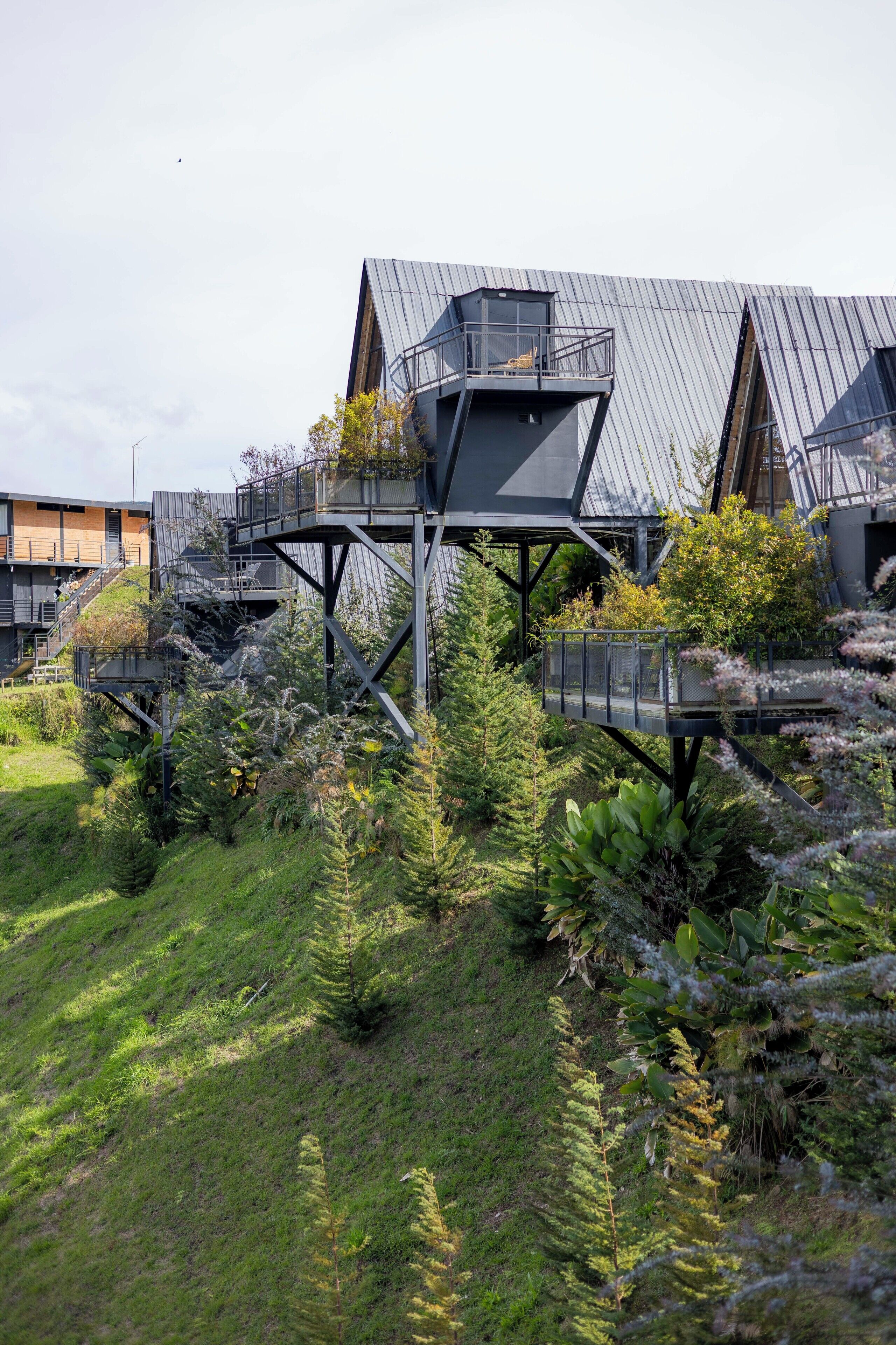 A modern building with a unique architectural design featuring a central elevated structure with balconies, surrounded by lush greenery.