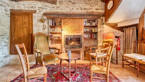 A rustic room with exposed stone walls, wooden beams, a fireplace, bookshelves, and traditional furniture.