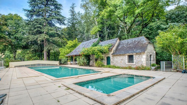 A pool area with two rectangular pools, stone buildings, and surrounding greenery.