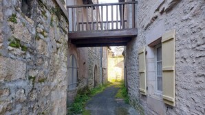 A narrow alleyway with stone walls, a wooden balcony, and a window with shutters.