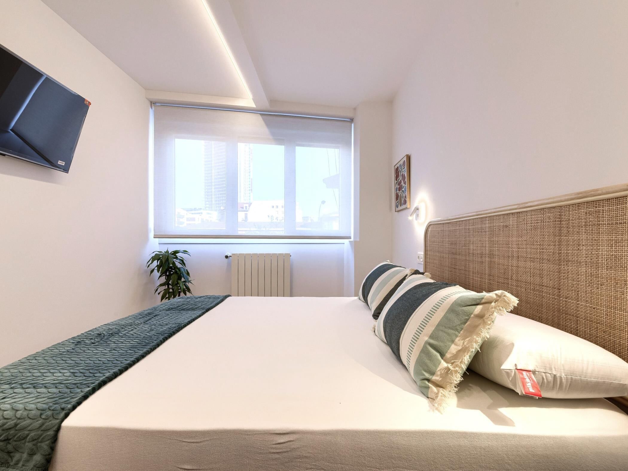 Een slaapkamer met een bed, een radiator, een raam en een plant.