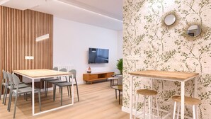 Un espace de bureau moderne avec un mur lambrissé en bois, une longue table entourée de chaises, un téléviseur fixé au mur et un papier peint à motifs agrémenté de deux miroirs.
