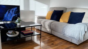 A modern living room with a flat-screen TV, a coffee table, and a grey sofa with blue and yellow cushions. - Luxurious Home Near Luton Airport. Suitable for Families and Contractors (Luton)