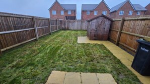 A backyard with a wooden fence, a shed, and a trash bin. - Luxurious Home Near Luton Airport. Suitable for Families and Contractors (Luton)