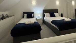 A bedroom with two beds, a nightstand, a desk, and a mirror. - Luxurious Home Near Luton Airport. Suitable for Families and Contractors (Luton)