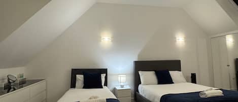 A bedroom with two beds, a nightstand, a desk, and a mirror.