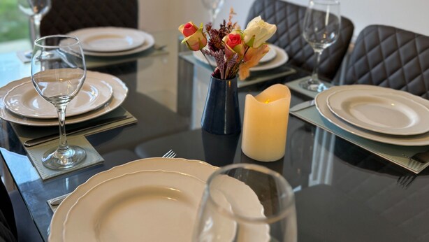 A dining table set with plates, glasses, and a vase with flowers. - Luxurious Home Near Luton Airport. Suitable for Families and Contractors (Luton)