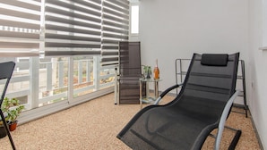 A balcony with a black lounge chair, a small table with a bottle and glasses, and a view of a construction site. - 2 bedroom awesome apartment in Vir (Vir)