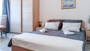 A neatly made bed with white and dark blue bedding, a wooden headboard, and a painting of a ship on the wall. - 2 bedroom awesome apartment in Vir (Vir)