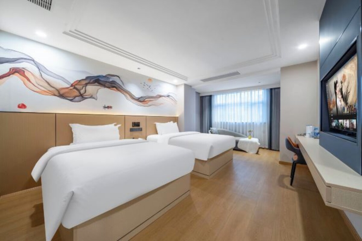 Habitación de hotel con dos camas, un escritorio, una silla y un ventanal grande.