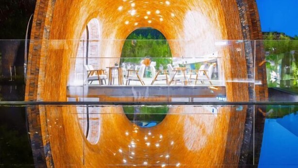 Una estructura circular de madera con piso de vidrio que refleja el interior, y un área de descanso con mesas y sillas.