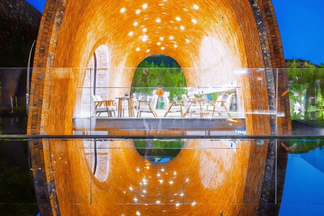 A circular structure with a reflective interior, possibly a water feature or a tunnel, with a view of outdoor seating and greenery.