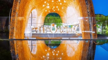 A circular structure with a reflective interior, possibly a water feature or a tunnel, with a view of outdoor seating and greenery.