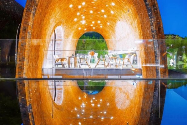 A circular structure with a reflective interior, possibly a water feature or a tunnel, with a view of outdoor seating and greenery.