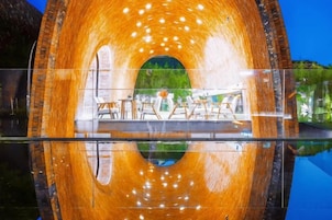 Una estructura circular con interior reflectante, posiblemente una fuente de agua o un túnel, con vistas a un área de estar al aire libre y follaje.