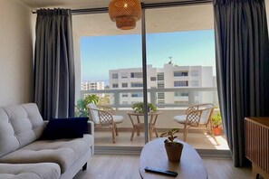 Un salon moderne avec un canapé, une table basse et un balcon agrémenté de fauteuils en osier et de plantes en pot.